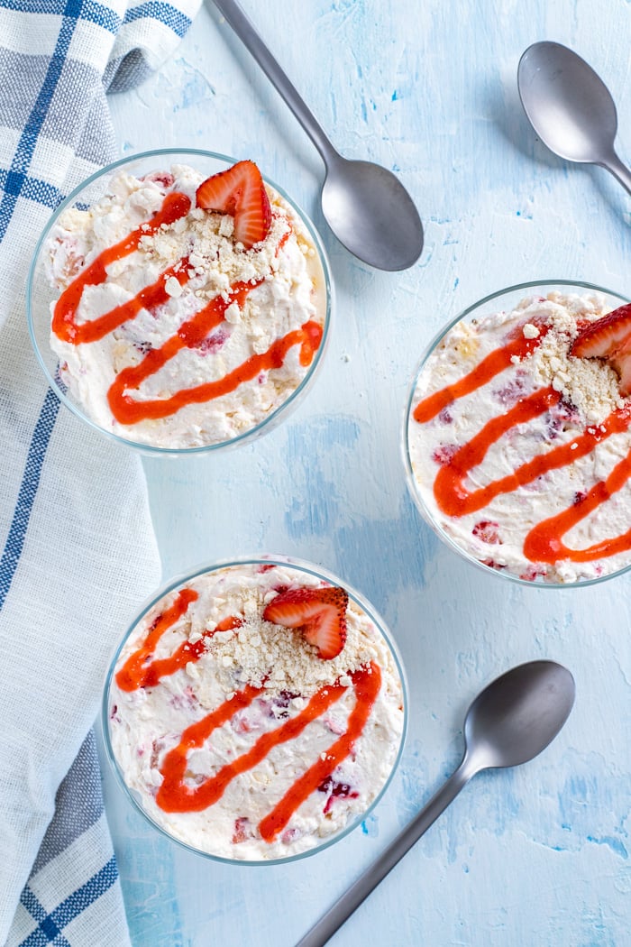 Strawberry sauce drizzled on top of three cream desserts with spoons lying beside the dishes