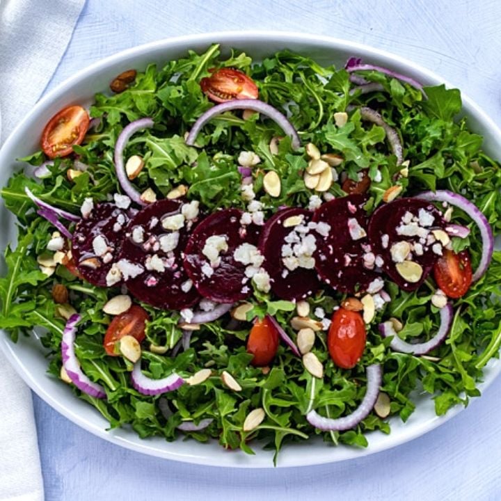 Sliced beets almon slivers and crumbled goat cheese on a bed of arugula | Irish American Mom Sliced beets, crumbled cheese and almonds on a green salad served on a platter
