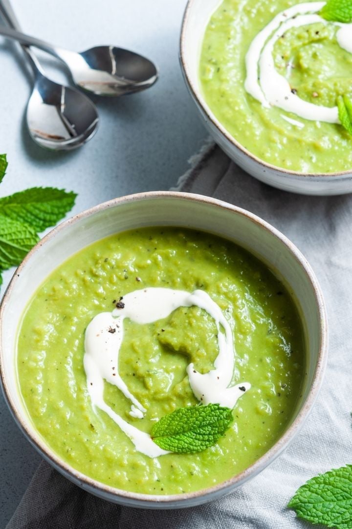Two bowls of pea and mint soup with a swirl of cream as garnish | Irish American Mom two bowls of green soup with cream swirl and green leaf garnish