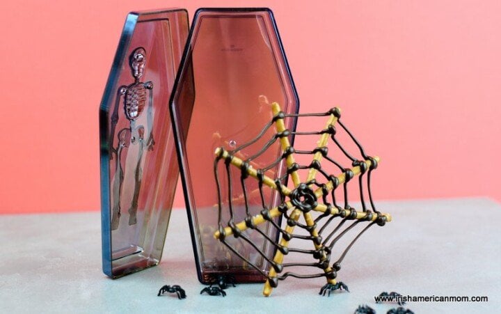 Edible spider webs made with chocolate and pretzel sticks | Irish American Mom Decorative skeleton coffin beside a candy and pretzel spider web