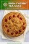 Round traditional Irish cherry tea cake topped with bright red cherries on parchment paper, promoting a classic homemade dessert recipe.