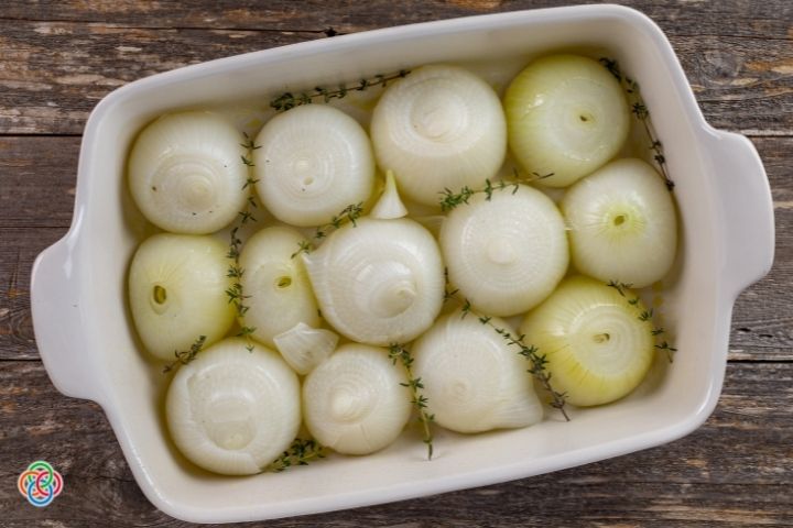 Adding thyme sprigs to parboiled onion halves in a casserole dish | Irish American Mom Thyme sprigs and onions in a casserole dish