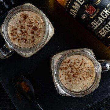 Overhead shot of milk punch in glasses with nutmeg garnish beside a bottle of whiskey