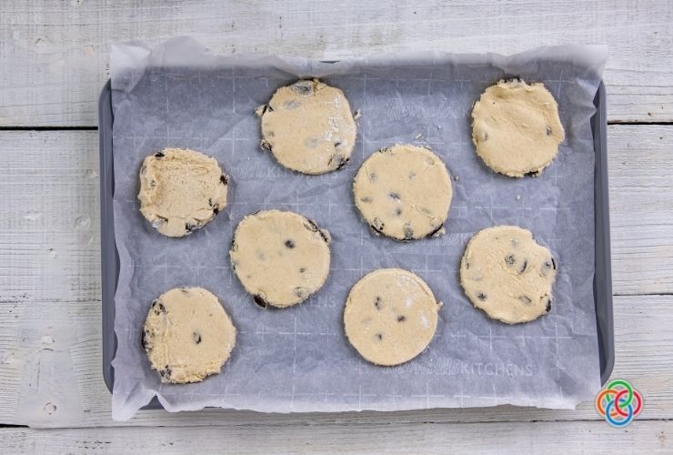 Unbaked Easter biscuits dough rounds on a baking tray lined with parchment paper | Irish American Mom Raisin cookie dough circles on a baking tray