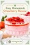 A glass dessert dish filled with creamy pink strawberry mousse, topped with whipped cream, strawberry sauce, and fresh diced strawberries. The elegant homemade dessert is displayed with fresh strawberries in the background and is perfect for summer entertaining or special occasions.