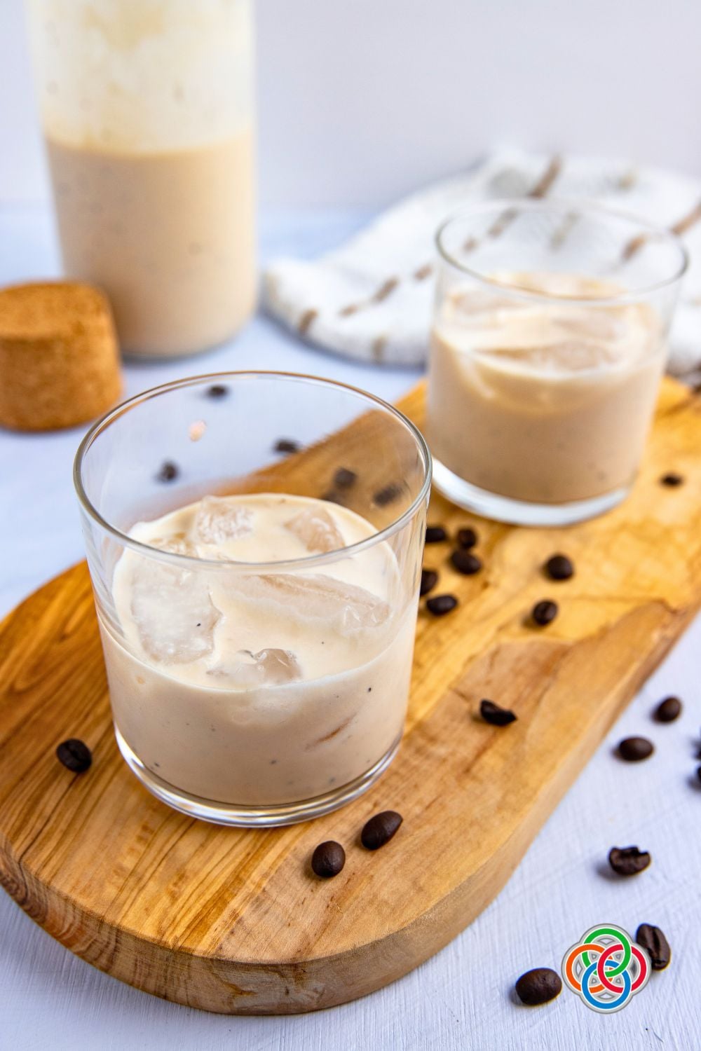 Glasses of creamy liqueur on a wooden board with coffee beans plus a bottle of the drink.