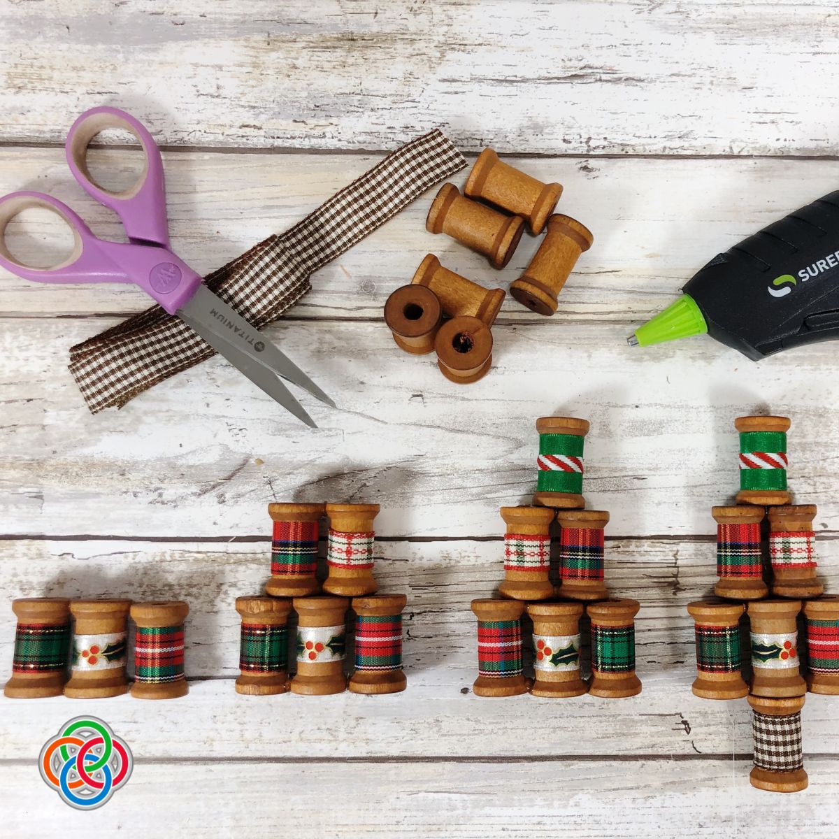 Assembling a sewing spool Christmas tree ornaments | Irish American Mom Stacked wooden spools with ribbons with a scissors and glue gun