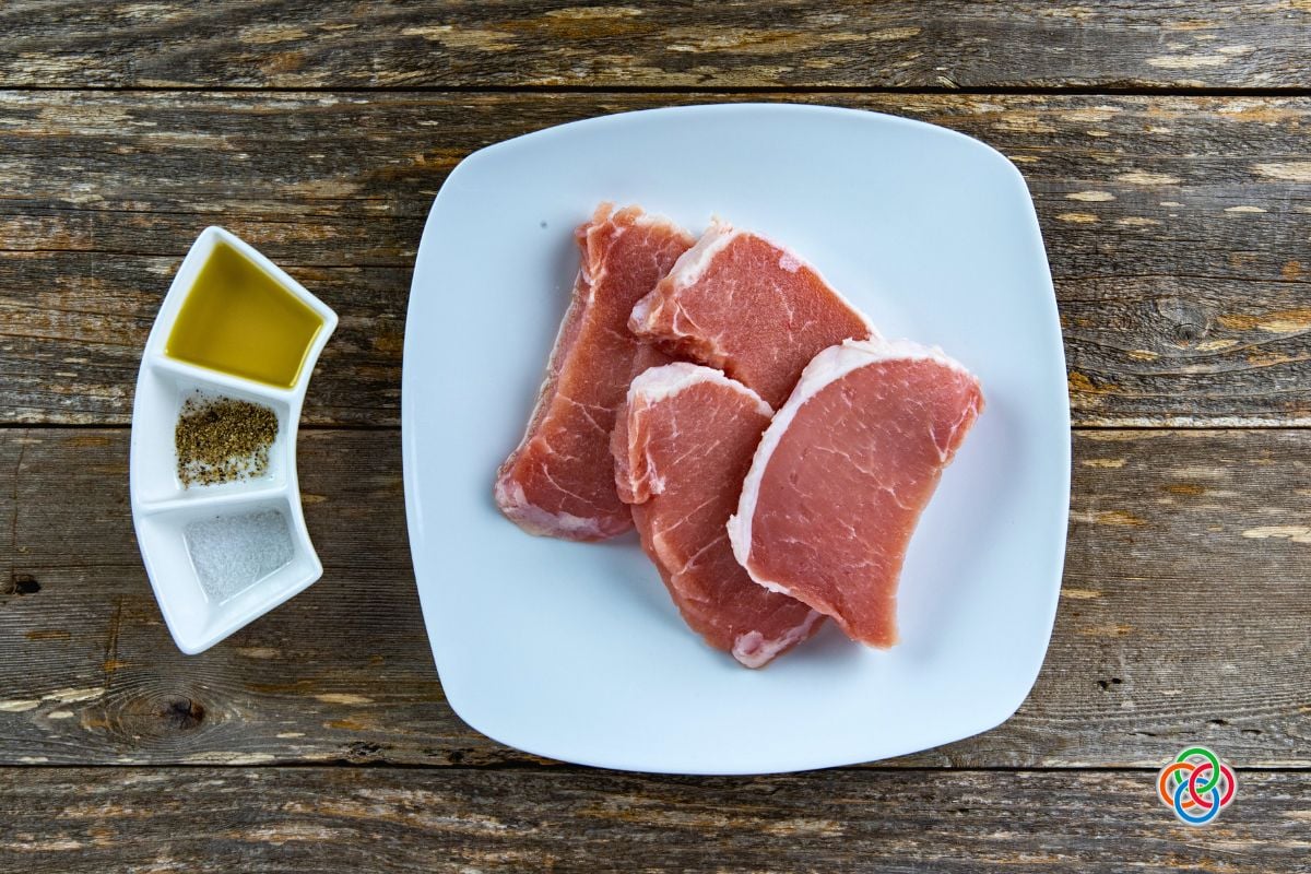 Ingredients for pan fried pork chops | Irish American Mom Raw pork chops on a plate beside a container with oil, salt and pepper