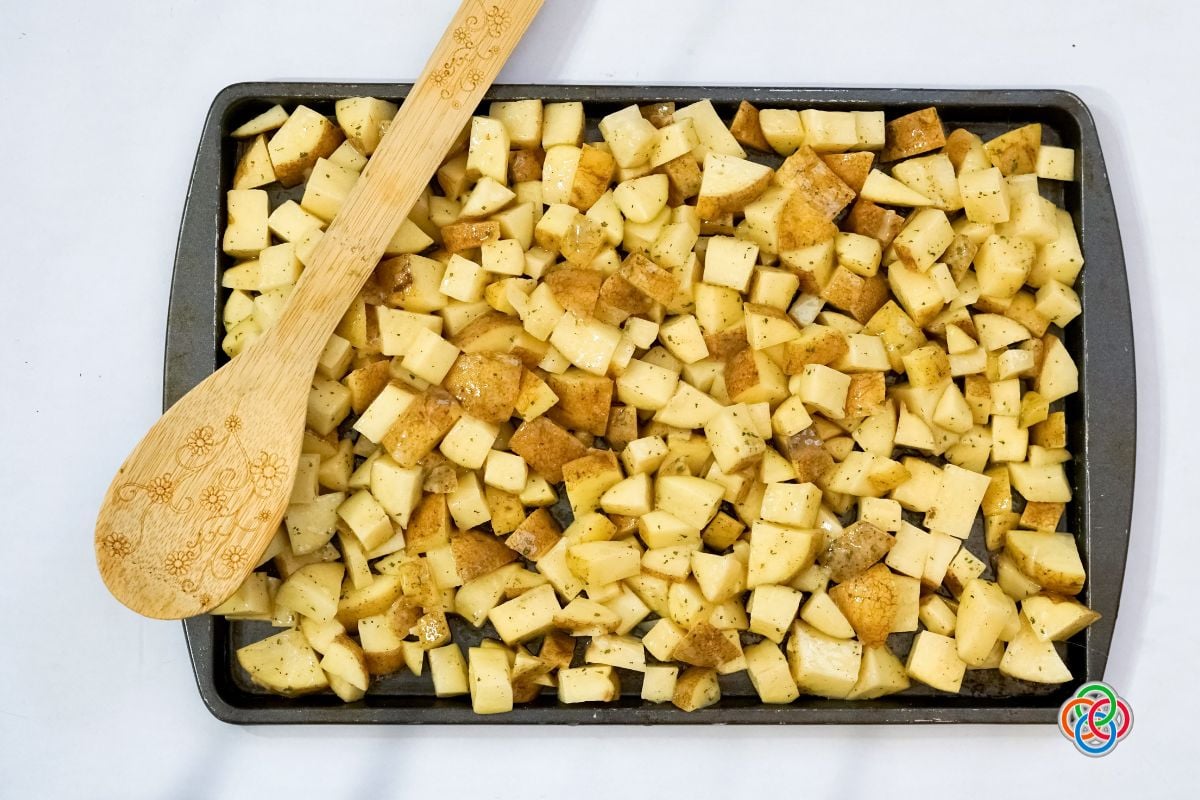 Diced potatoes on a sheetpan with a wooden spoon