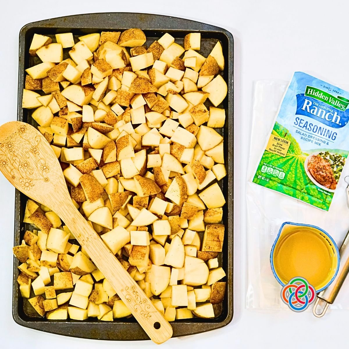 Diced potatoes on a sheetpan with a wooden spoon plus olive oil and ranch seasoning