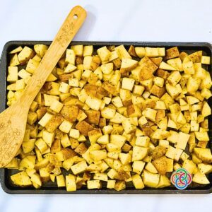 Chopped potatoes on a sheetpan with a wooden spoon