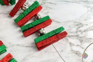 Threading glitter clothespins and bells onto a wire
