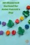 Pinterest graphic reading “3D Shamrock Garland for Saint Patrick’s Day” featuring green 3D shamrocks and colorful rainbow paper balls attached to white string on a blue background, with Irish American Mom logo in the corner.