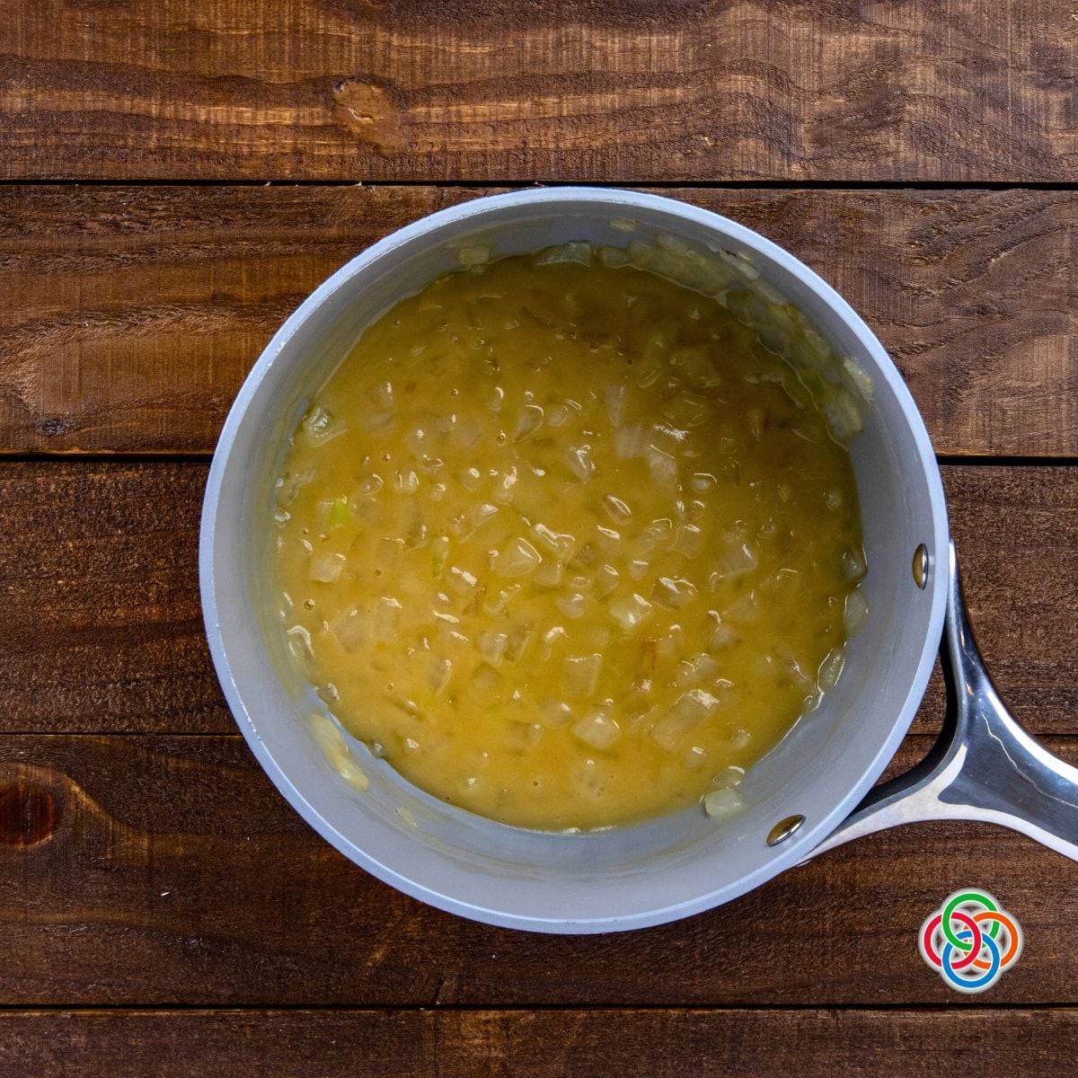Overhead view of creamy whiskey onion sauce simmering in a saucepan on a wooden table background.