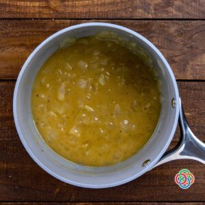 Overhead view of creamy whiskey onion sauce with visible onion pieces simmering in a saucepan on a wooden table.