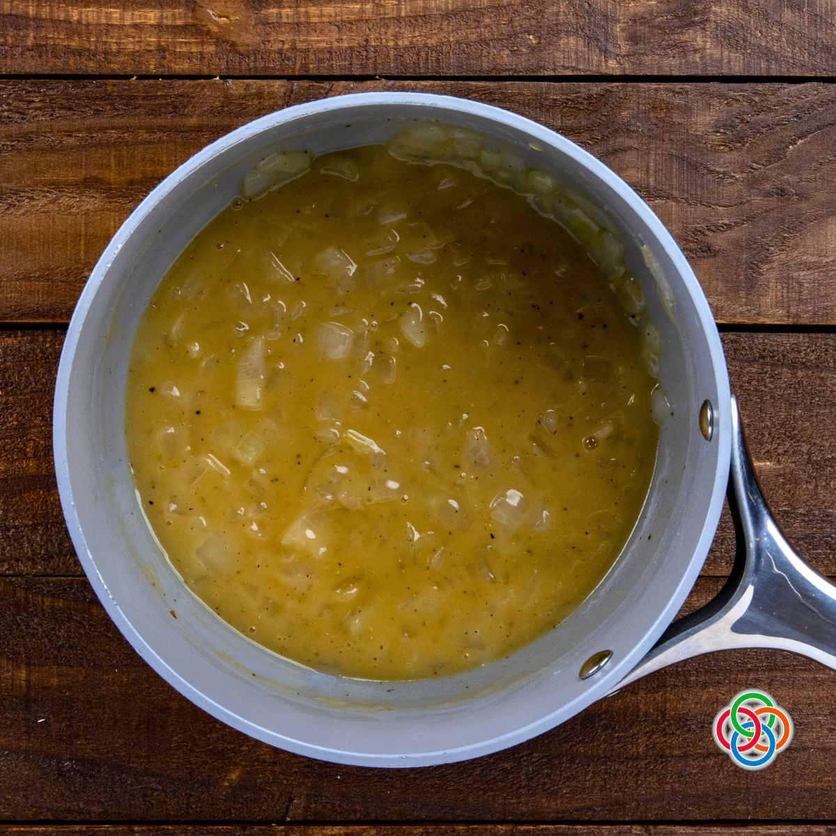 Overhead view of creamy whiskey onion sauce with visible onion pieces simmering in a saucepan on a wooden table.