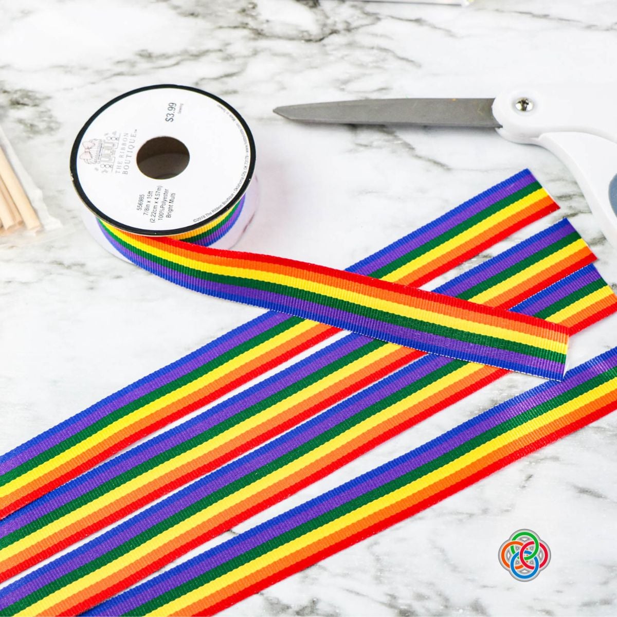 Cutting ribbon strips for a shamrock wand craft | Irish American Mom Close-up of a glittery green foam shamrock with rainbow ribbon strips and a wooden dowel attached using glue dots, shown during the assembly of a Saint Patrick's Day wand craft.