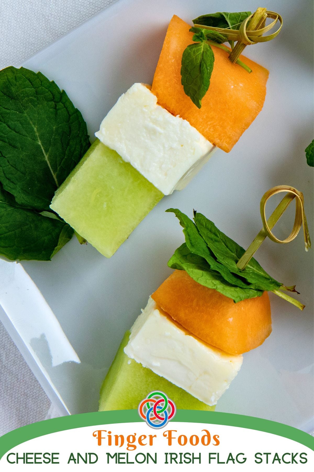Irish flag appetizer stacks made with honeydew, feta cheese, and cantaloupe cubes, topped with fresh mint and secured with decorative cocktail sticks on a white platter.