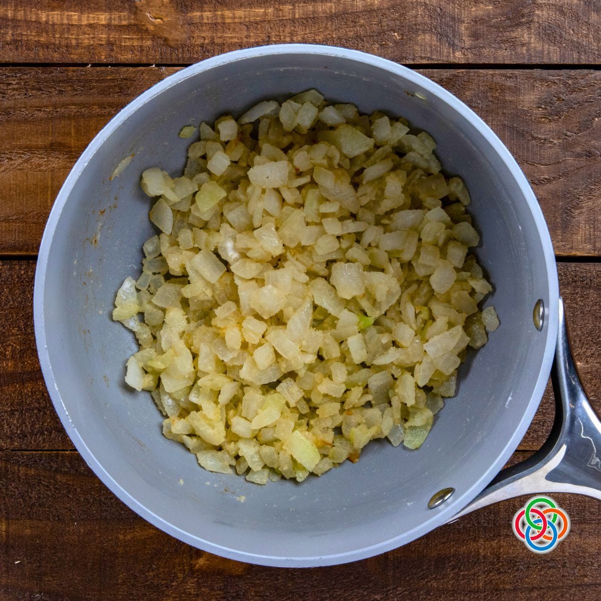 Overhead view of sautéed onions mixed with flour in a saucepan, forming the base of a whiskey onion sauce on a wooden surface.