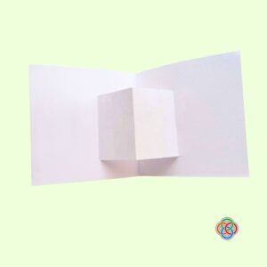 Folded socket for decoration for Pop Up Rainbow Card Craft | Irish American Mom Open white cardstock card showing the folded pop-up platform in the center, ready for decorating with a rainbow and pot of gold craft pieces.