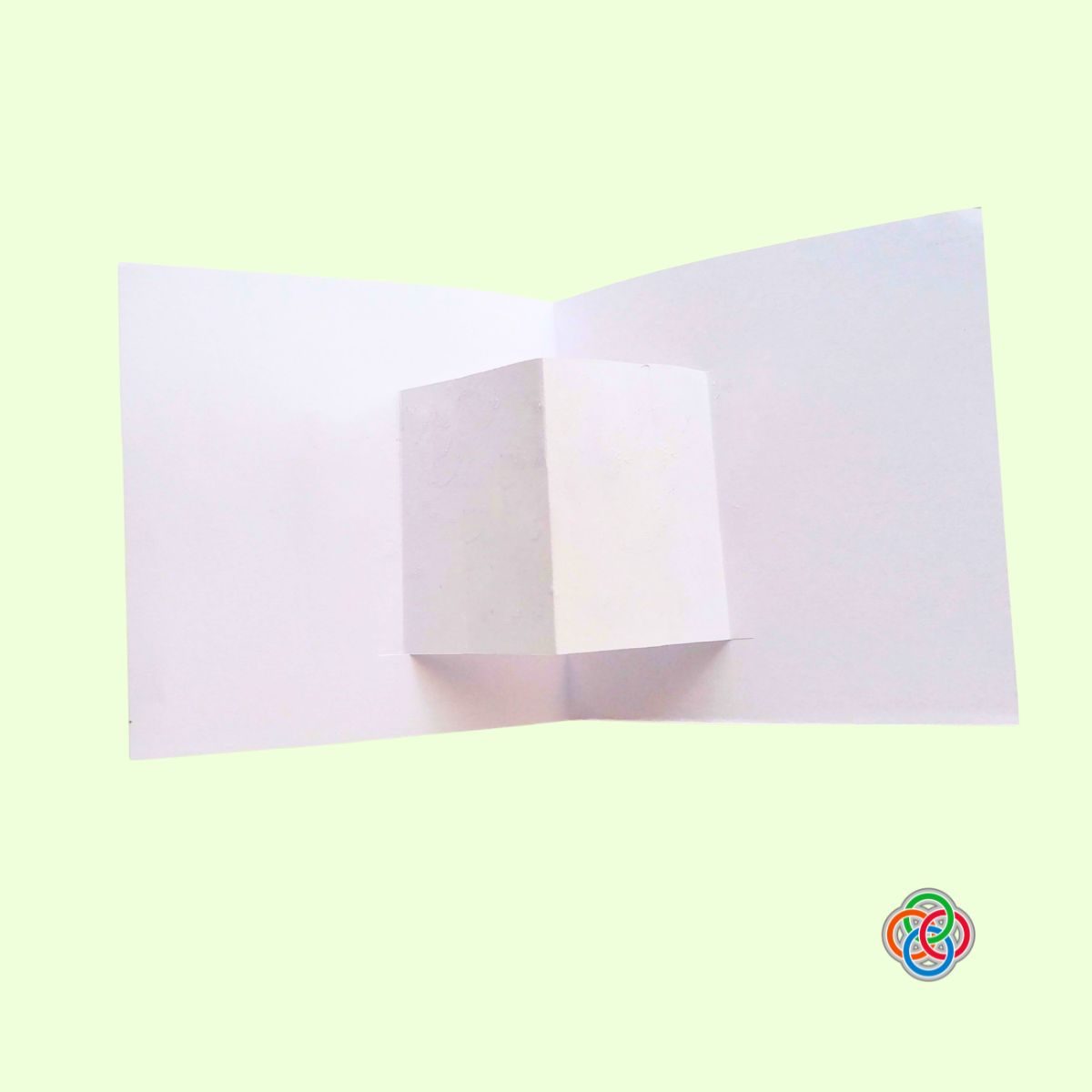 Folded socket for decoration for Pop Up Rainbow Card Craft | Irish American Mom Open white cardstock card showing the folded pop-up platform in the center, ready for decorating with a rainbow and pot of gold craft pieces.