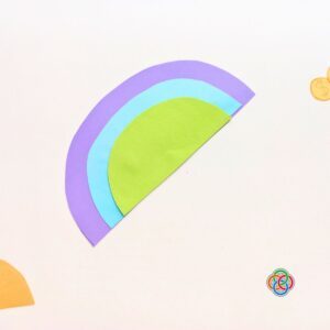 Glue rainbow pieces for Pop Up Rainbow Card Craft | Irish American Mom Layered purple, blue, and green paper rainbow pieces glued together for a Saint Patrick's Day pop up card craft on a white background.