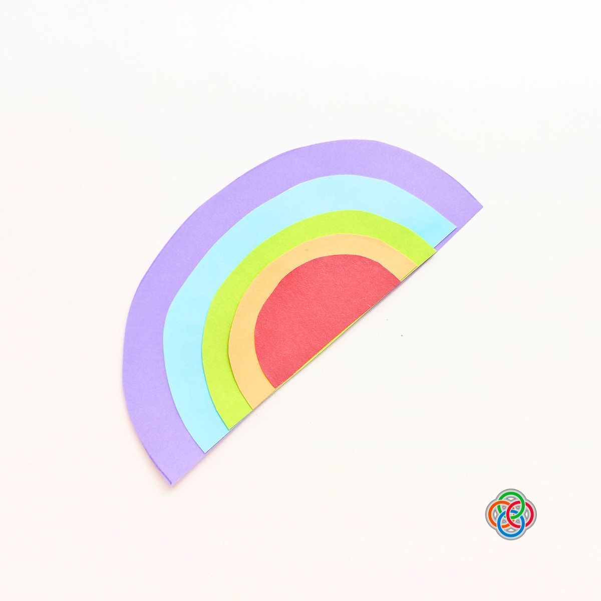 Glue rainbow pieces large to small for Pop Up Rainbow Card Craft | Irish American Mom Colorful layered paper rainbow glued from largest purple arc to smallest red arc for a Saint Patrick’s Day pop up card craft.