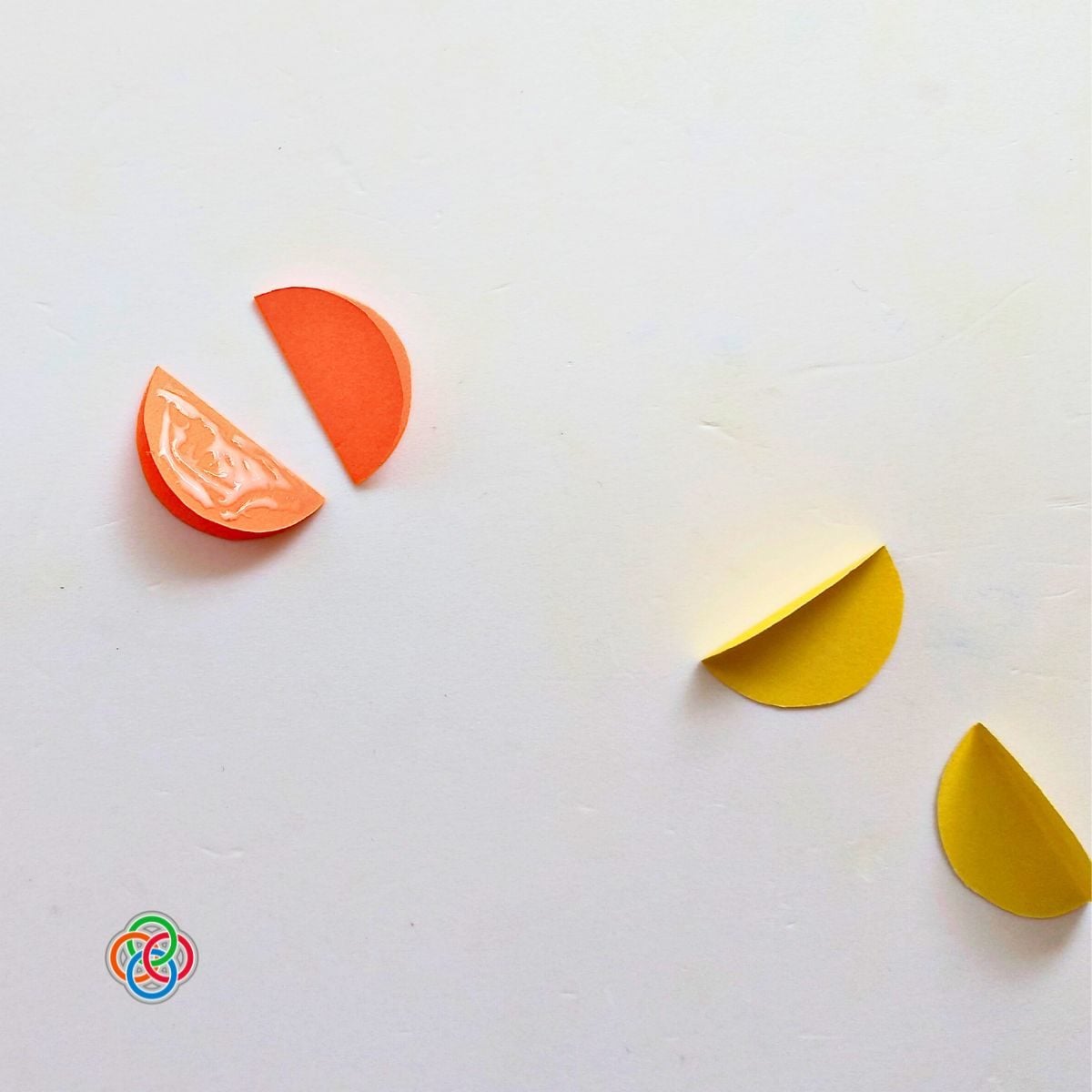 Folded orange and yellow paper circle pieces being glued side by side to form a 3D paper ball for a Saint Patrick’s Day garland craft, with Irish American Mom logo in the corner.