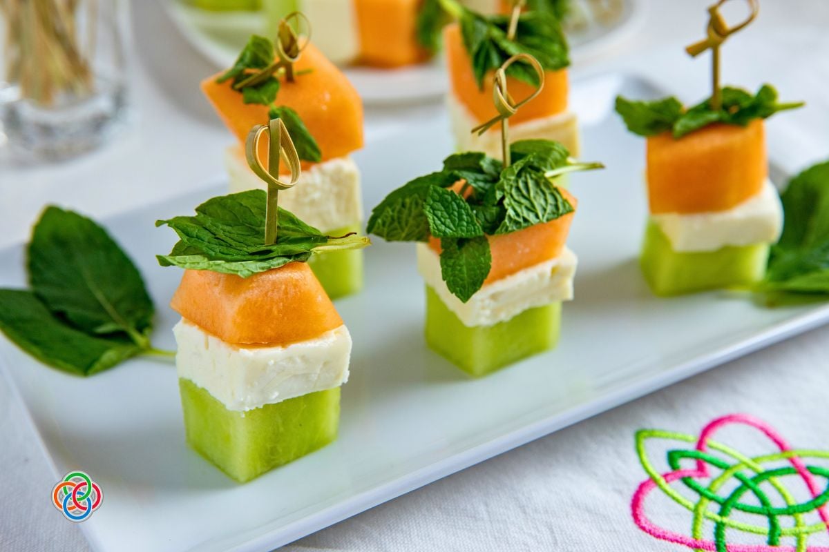 Irish flag appetizer stacks made with honeydew, feta cheese, and cantaloupe cubes topped with fresh mint and secured with decorative cocktail picks on a white serving platter.