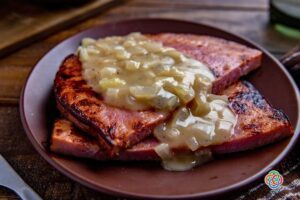 Pan-seared ham steaks topped with creamy whiskey onion sauce on a brown plate, served as a hearty Irish-inspired main course.