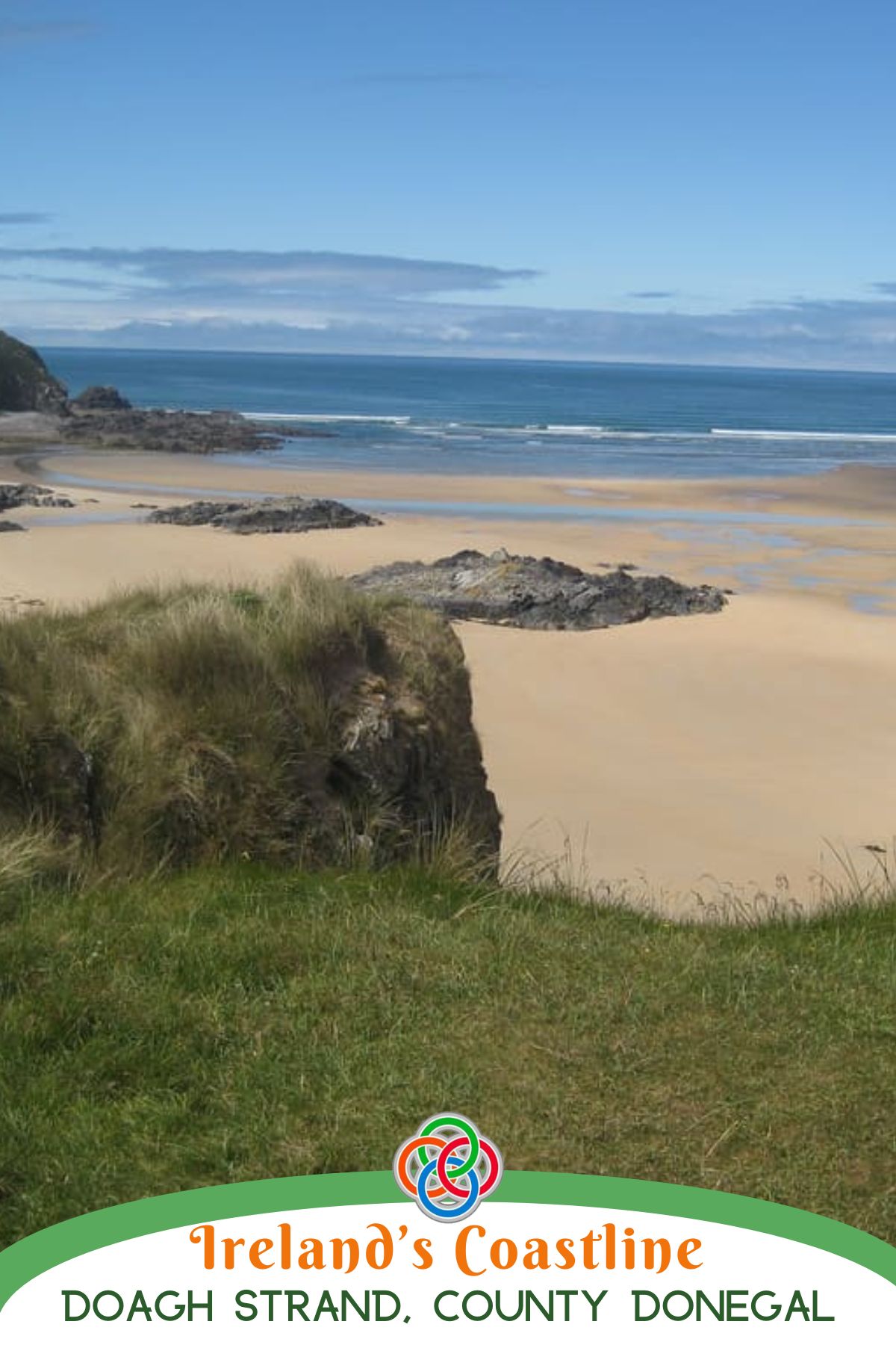 Sandy beach at Doagh Strand in County Donegal, Ireland, with grassy dunes in the foreground, rocky outcrops on the shore, and calm blue Atlantic waters under a wide sky.