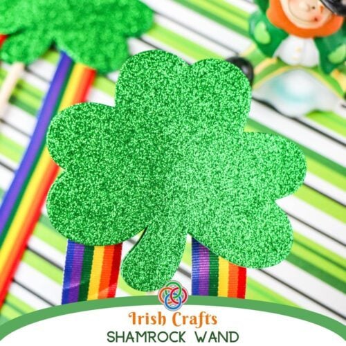 Irish Crafts Shamrock Wand | Irish American Mom Close-up of a glittery green shamrock wand with rainbow ribbon streamers on a green striped background, labeled