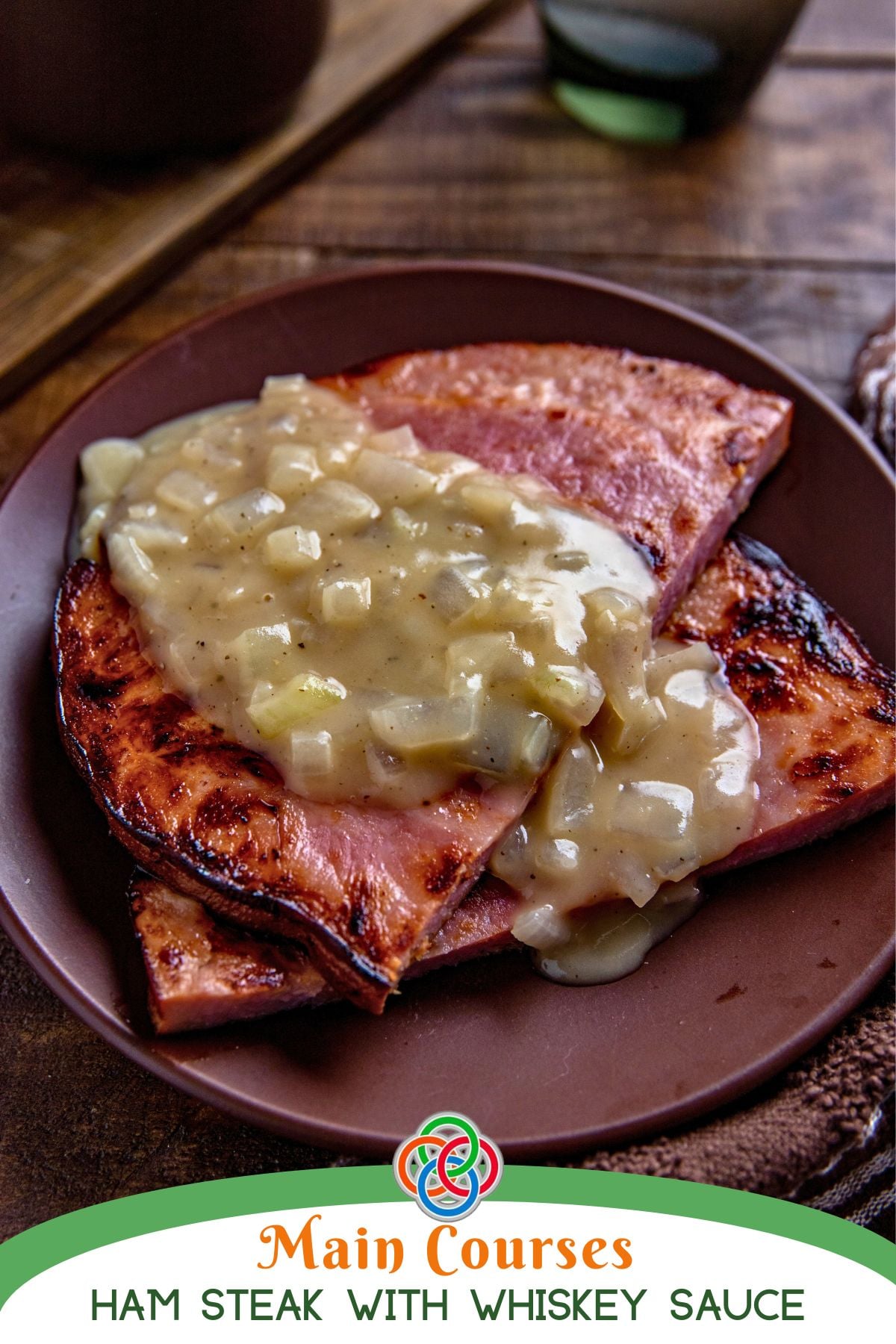 Pan-seared ham steaks topped with creamy onion whiskey sauce on a brown plate, styled for a main course Irish dinner.