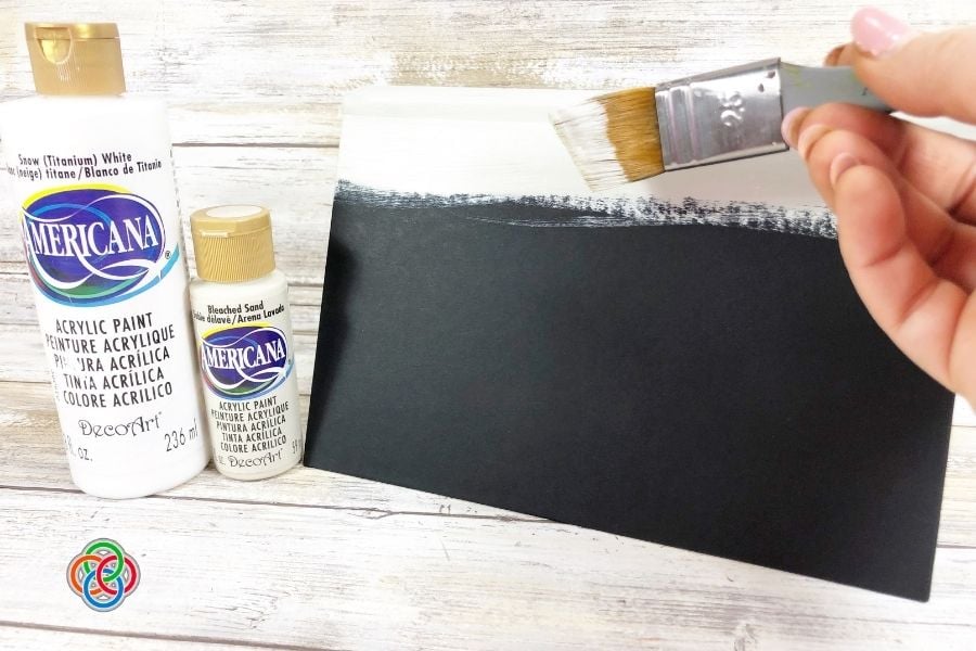 Painting the covers of old books for a | Irish American Mom Hand painting a dark hardcover book with white acrylic paint to create a farmhouse-style basecoat for a Saint Patrick's Day decorative book stack craft.