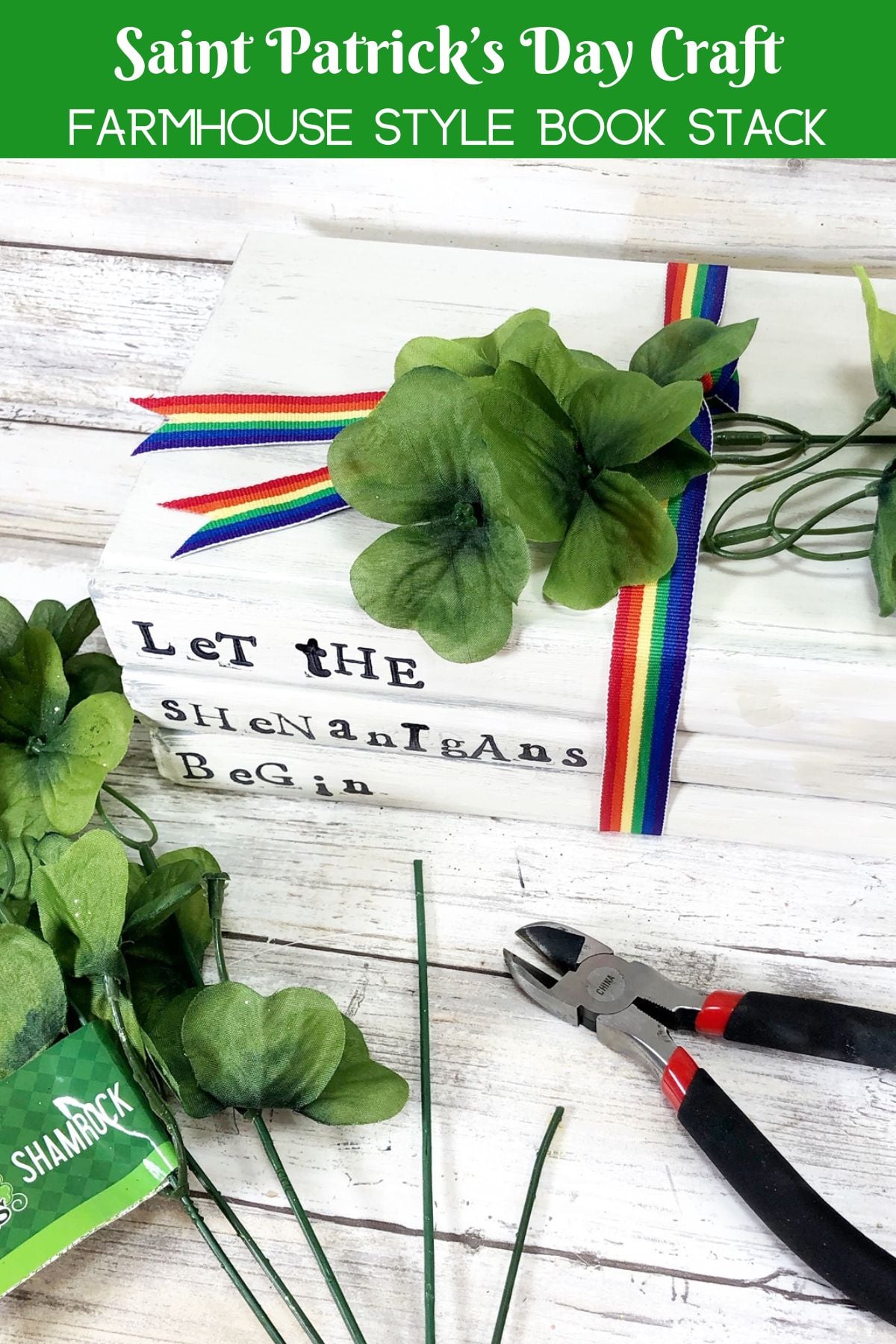Saint Patricks Day Craft Shamrock Farmhous | Irish American Mom Farmhouse style Saint Patrick’s Day book stack stamped “Let the Shenanigans Begin” tied with rainbow ribbon and decorated with green shamrocks, with craft supplies nearby.