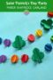 Pinterest graphic reading “Saint Patrick’s Day Party Paper Shamrock Garland” featuring 3D green shamrocks and colorful rainbow paper balls strung on white string against a blue background.