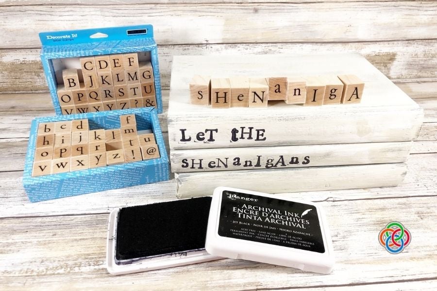 Stamping a message on book spines for a dec | Irish American Mom Alphabet stamps and black ink pad beside white painted books stamped with