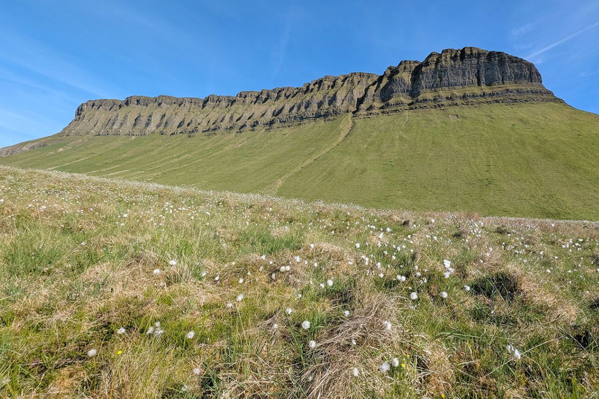 Ben Bulben County Sligo | Irish American Mom Benbulben mountain rising above grassy fields in County Sligo, Ireland, with its distinctive flat summit and steep limestone cliffs under a clear blue sky.