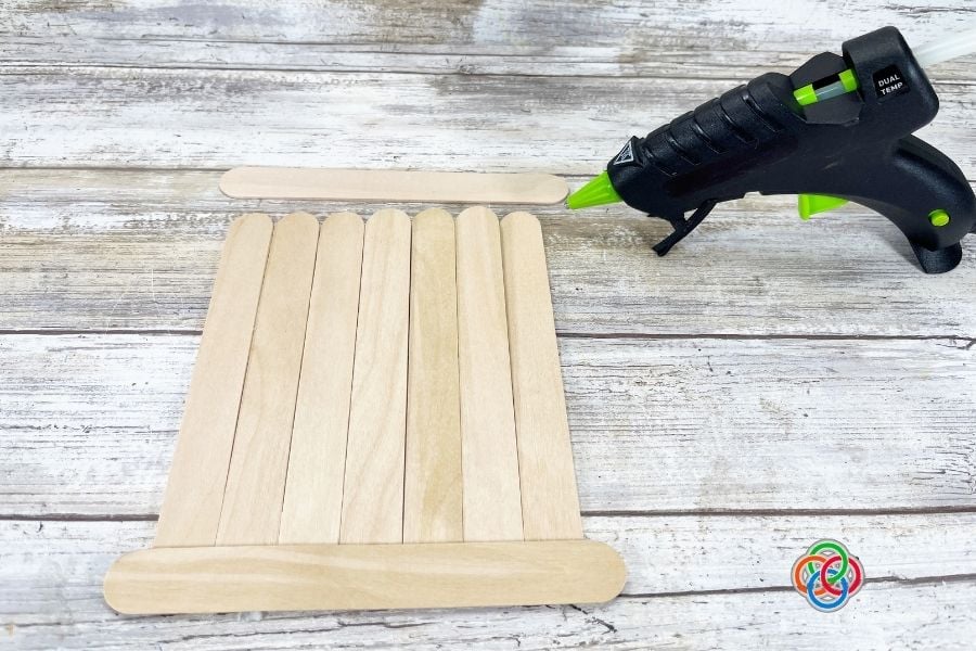 Jumbo craft sticks glued together to create a wooden sign base with a hot glue gun for a St. Patrick’s Day shamrock craft project.