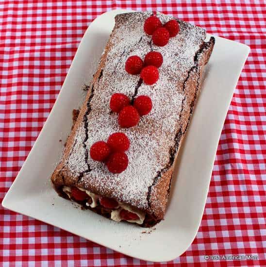 Chocolate roulade rolled with cream and raspberries, sliced to show spiral filling.