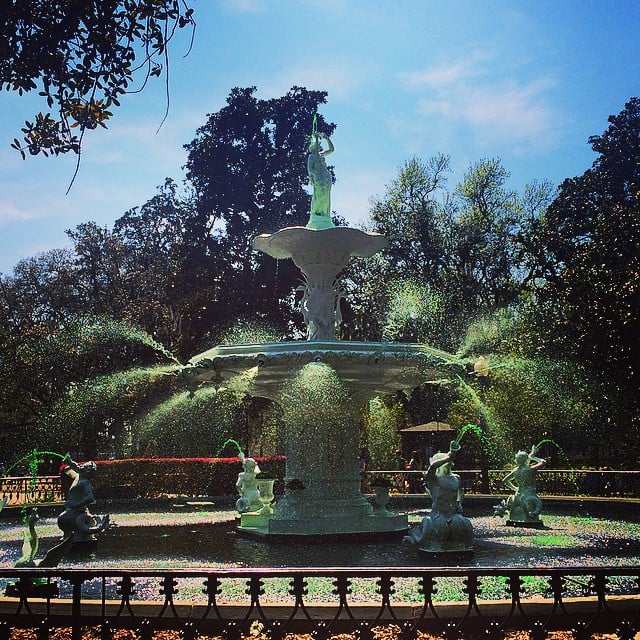 City fountain with dyed green water spouting in a tree lined park