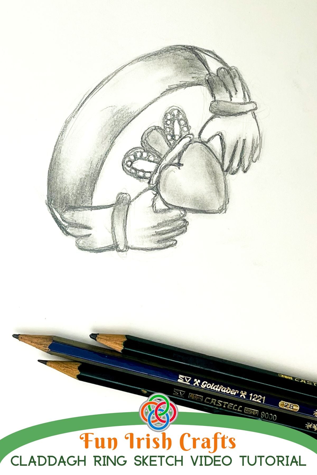 Shaded pencil drawing of a Claddagh ring with heart, crown, and hands on white paper beside graphite pencils, with text reading 