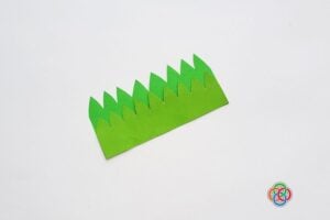 Layered green paper grass pieces glued together to form a pocket base for a paper tulip craft on a white background.