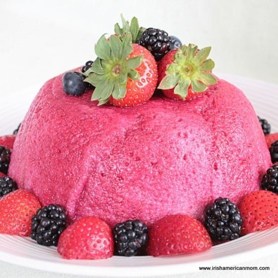 Molded summer pudding made with fresh berries and bread, sliced to reveal vibrant red and purple fruit filling.