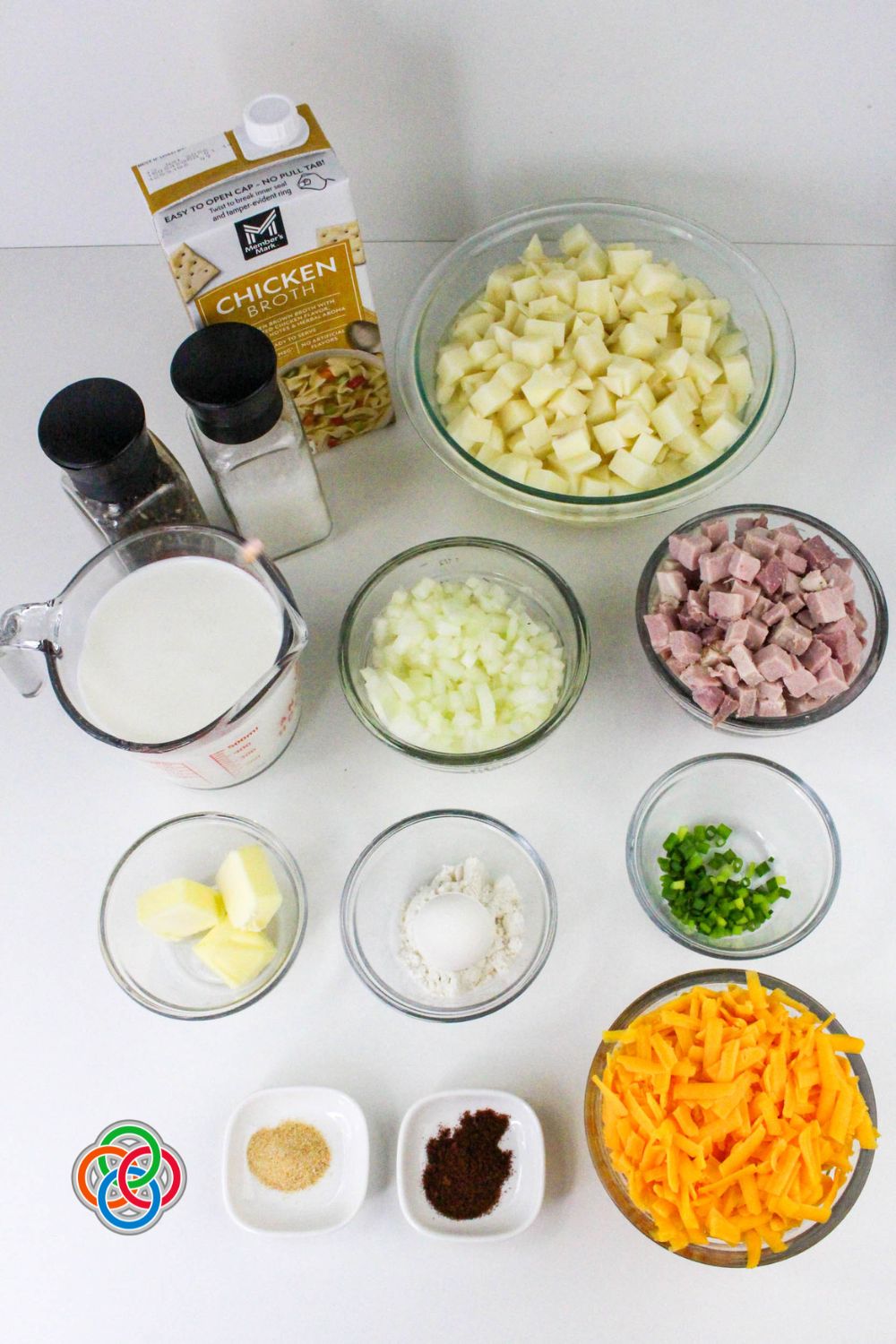Ingredients laid out for cheddar ham and potato soup including diced potatoes, ham, shredded cheese, milk, butter, flour, onion, chicken broth, and seasonings.