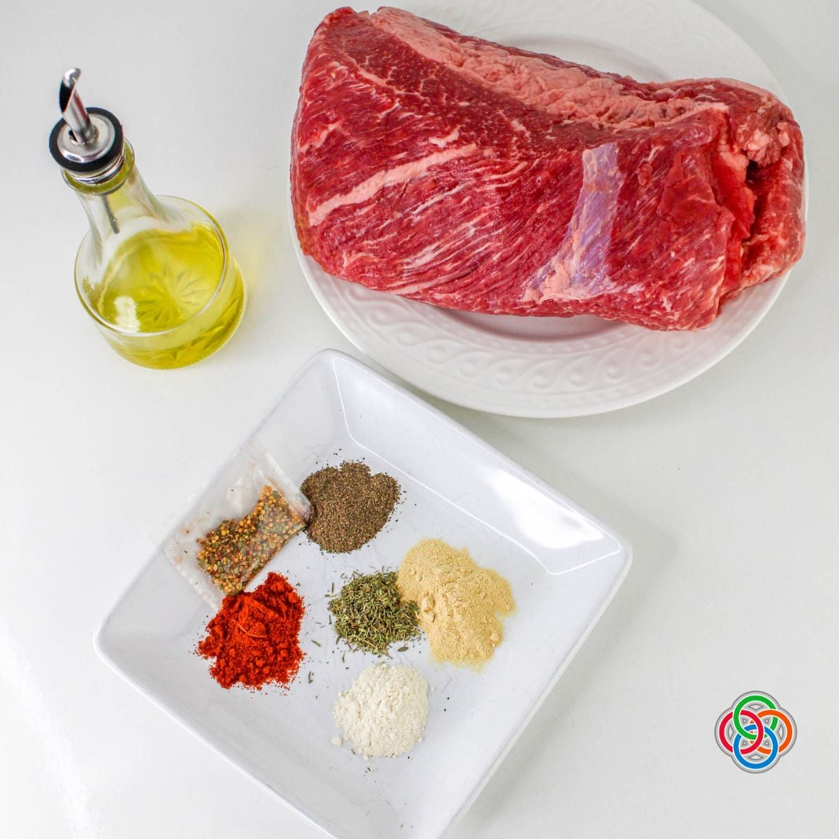 Corned beef brisket uncooked beside a plate of spices and a bottle of olive oil with a Celtic logo