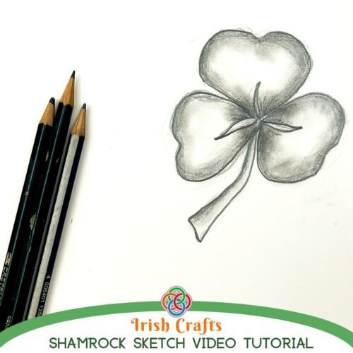 Shaded pencil drawing of a three-leaf shamrock with stem on white paper beside graphite pencils, with text reading 