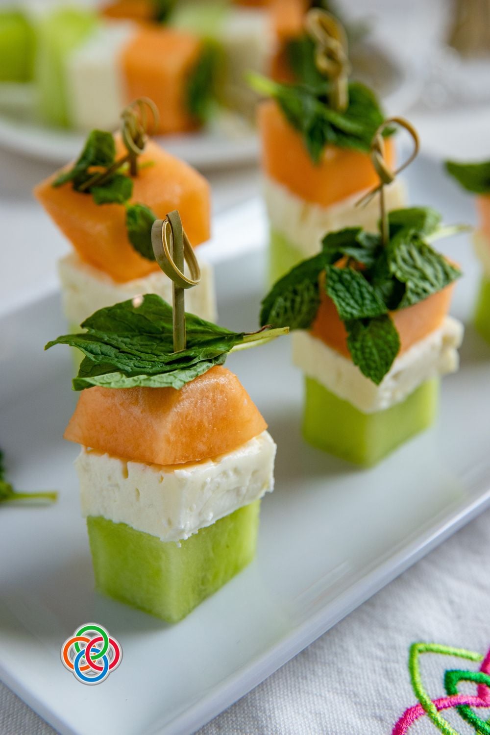 Close-up of Irish flag appetizer stacks made with honeydew, feta cheese, and cantaloupe cubes topped with fresh mint leaves and secured with decorative cocktail sticks on a white platter.