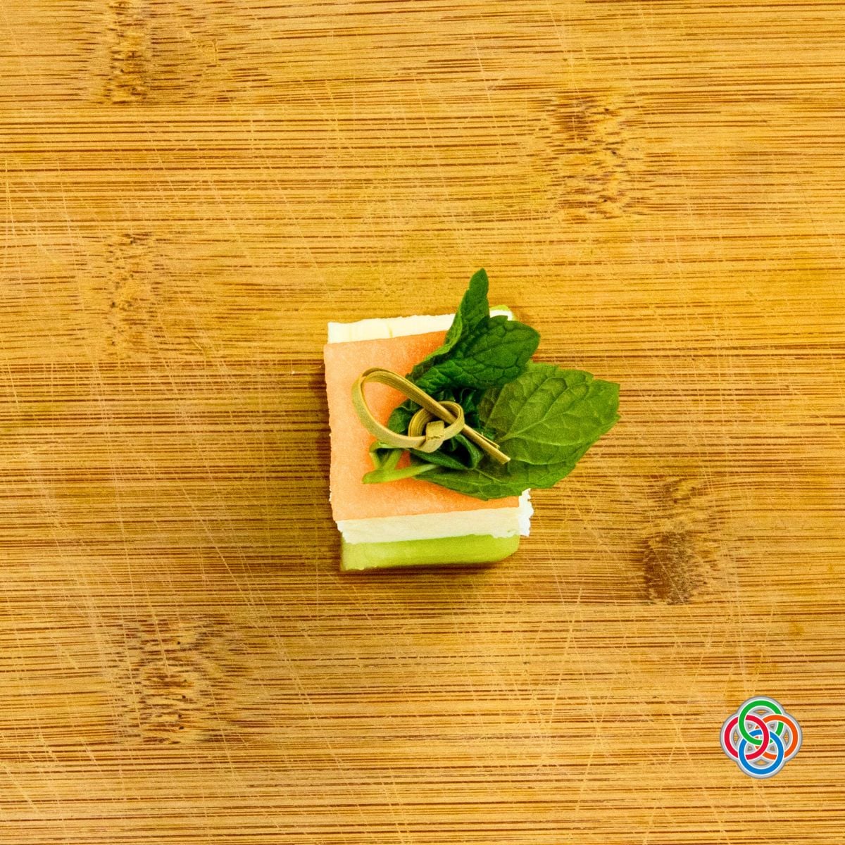 Overhead view of an Irish flag appetizer stack made with honeydew, feta, and cantaloupe topped with fresh mint leaves and secured with a decorative cocktail stick on a wooden board.