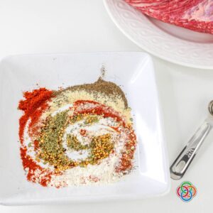 Plate with mixed spices including paprika, garlic powder, onion powder, thyme, and pepper used to create a homemade seasoning rub for corned beef brisket.